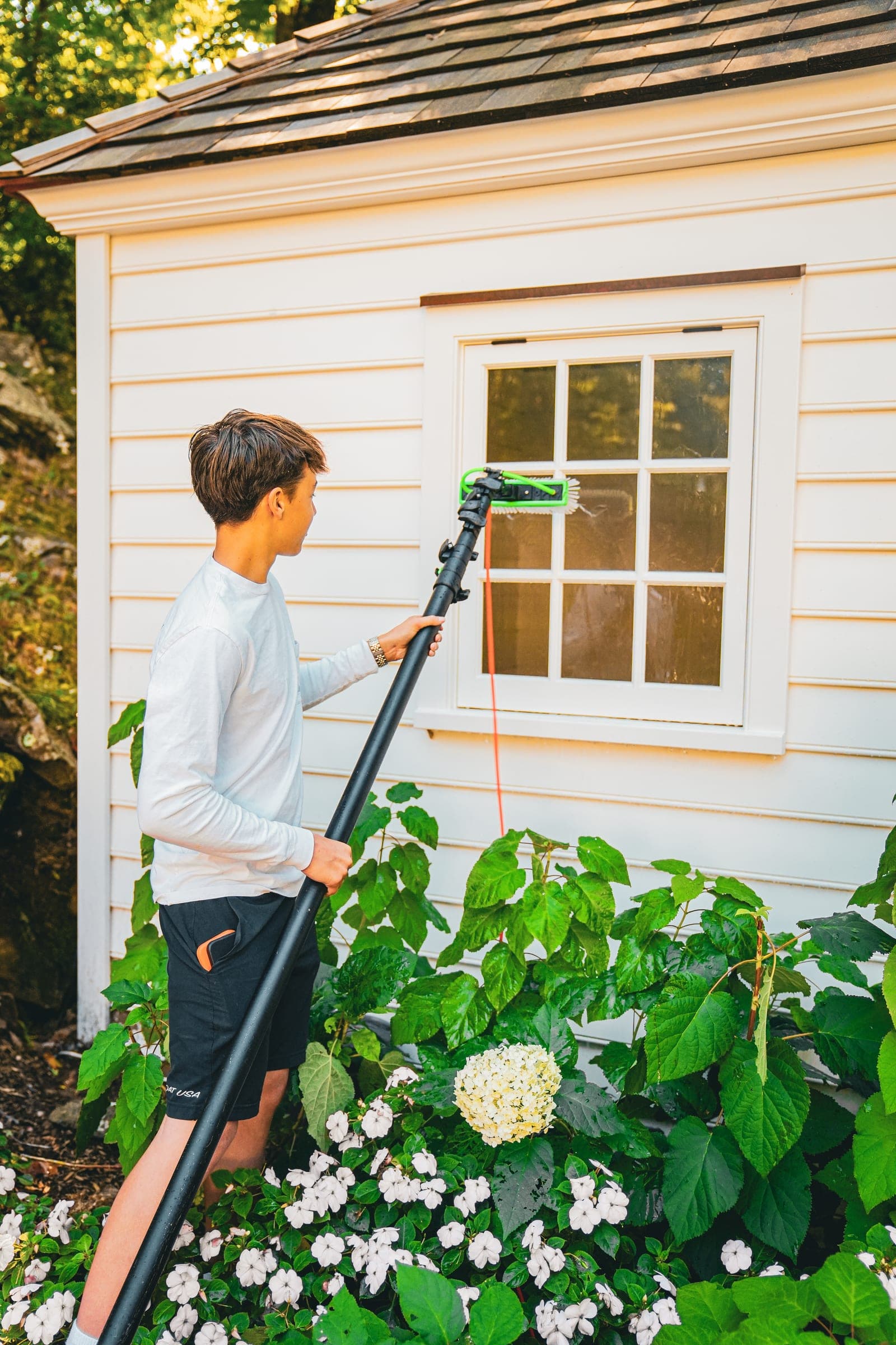 Cleaner washing a cottage window above white hydrangeas